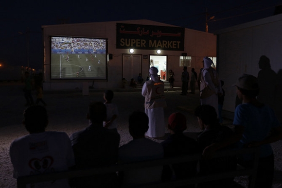 UAE Red Crescent members and Syrian refugees watch the World Cup soccer match between Argentina and Switzerland on a large screen after taking their meals for iftar during Ramadan at the Mrajeeb Al Fhood refugee camp