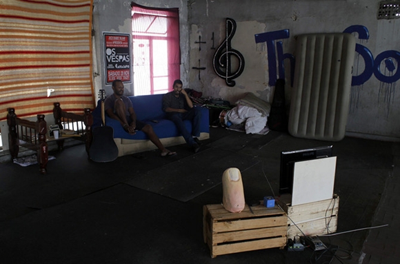 Grey and Alan, local dwellers, who live as squatters in an abandoned office building, watch a soccer match between Australia and the Netherlands in the centre of Sao Paulo